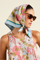Woman wearing a floral headscarf and sunglasses against a beige background