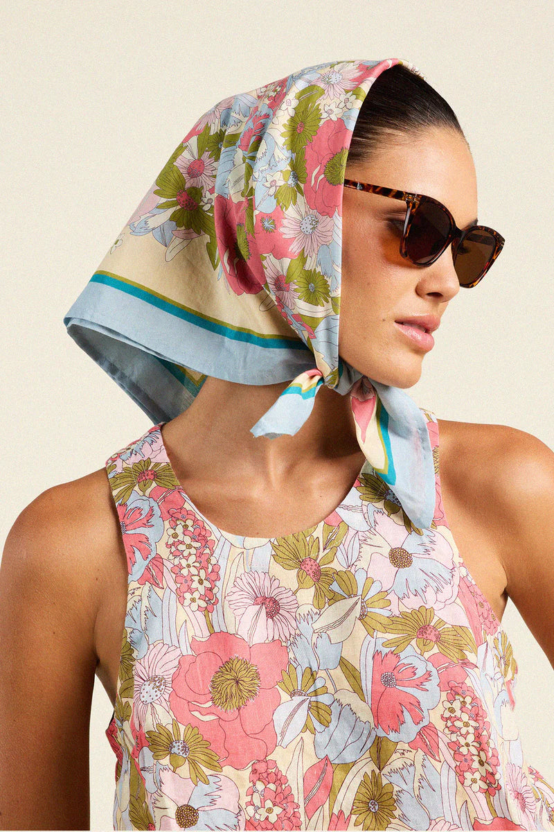 Woman wearing a floral headscarf and sunglasses against a beige background