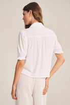 Woman wearing a white blouse with short sleeves on a plain background
