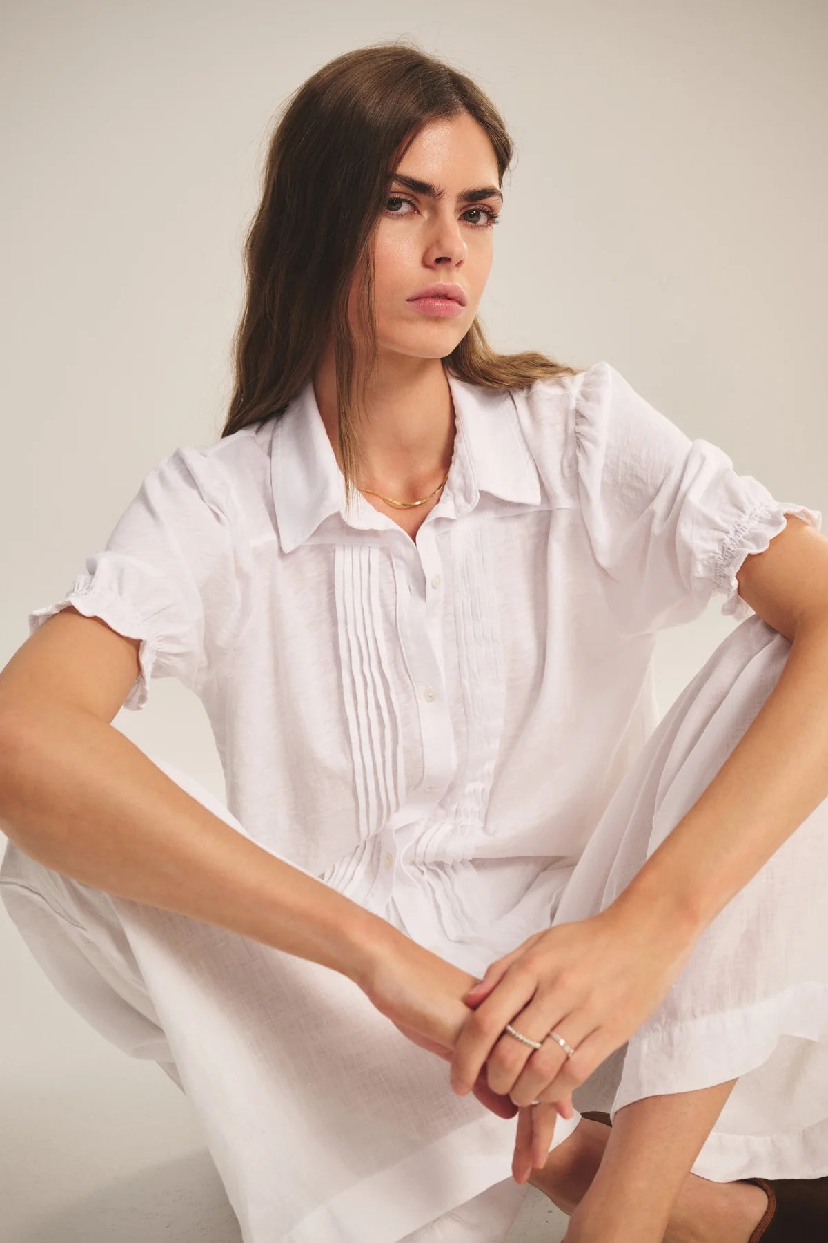 Woman wearing a white dress sitting against a plain background