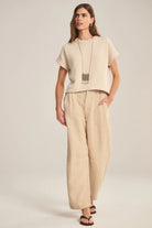 Woman wearing a beige top and wide-leg pants on a plain background