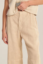 Person wearing beige pants and a cream top on a plain background