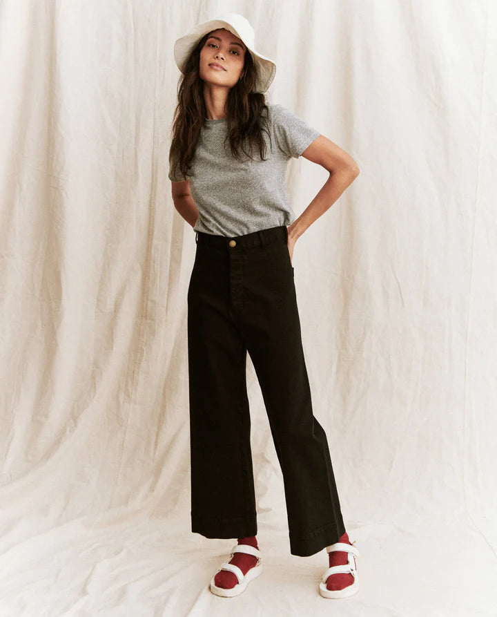 Woman wearing a gray t-shirt, black wide-leg pants, and a white hat against a plain background