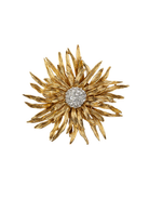 Gold flower-shaped brooch with a central gemstone on a white background