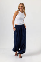 Woman wearing a white sleeveless top and navy wide-leg pants on a white background