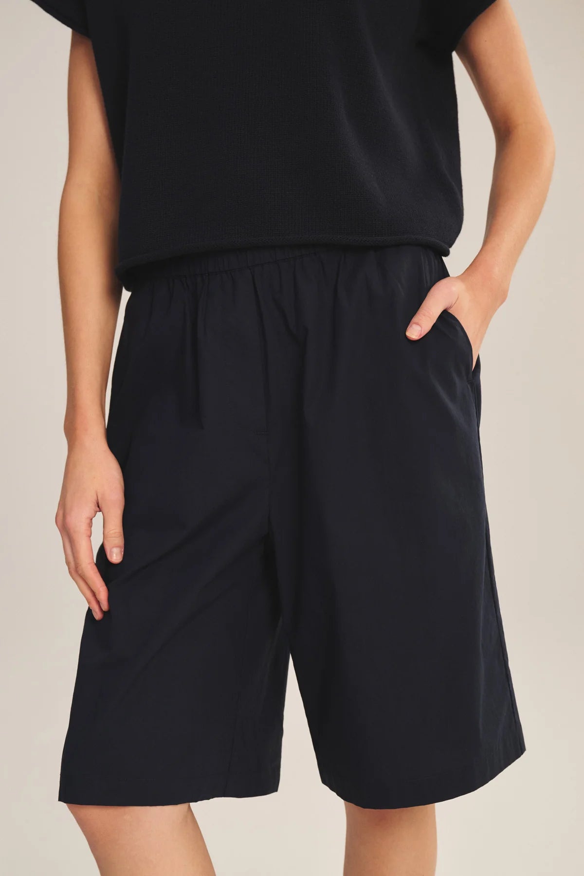 Person wearing black shorts and a black top on a neutral background