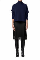 Person wearing a navy sweater and black skirt with sheer overlay on a white background
