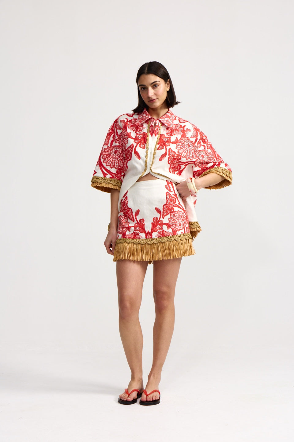 Woman wearing a red and white patterned top with gold accents on a white background