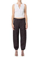 A model wearing dark brown baggy trousers with side cargo pockets, paired with a white sleeveless crop top and strappy heels, shown against a plain white background.