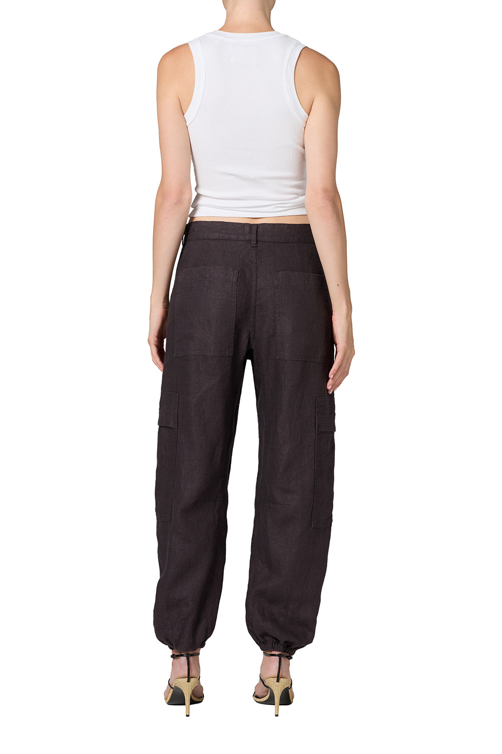 A model wearing dark brown baggy cargo pants with a white sleeveless crop top and strappy heels, shown against a plain white background.