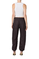 A model wearing dark brown baggy cargo pants with a white sleeveless crop top and strappy heels, shown against a plain white background.