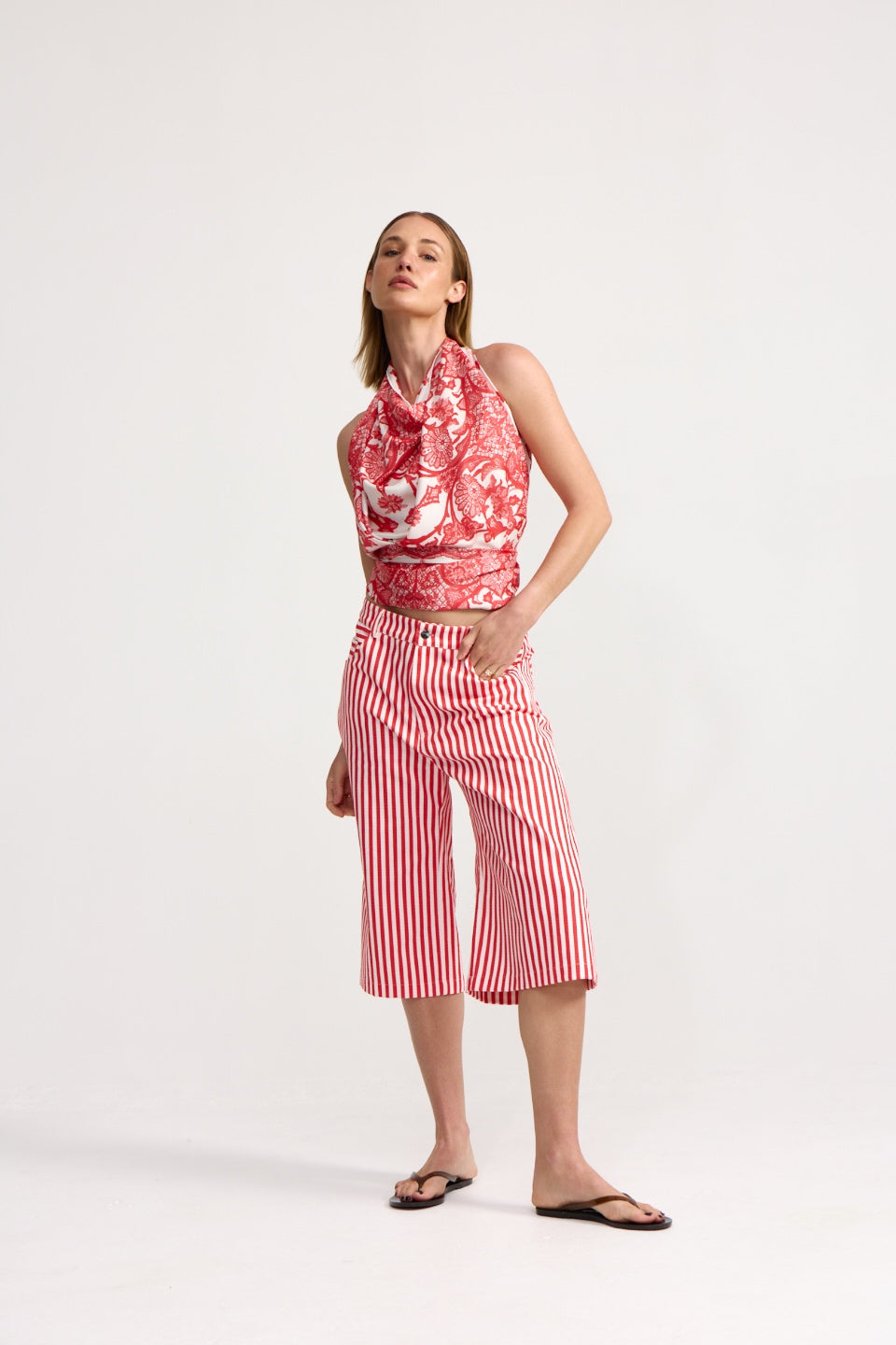 Woman wearing a red and white patterned sleeveless top and striped pants on a white background