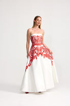 Woman wearing a strapless gown with red lace detailing on a white background