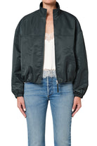 Person wearing a dark green jacket over a white top and blue jeans on a white background