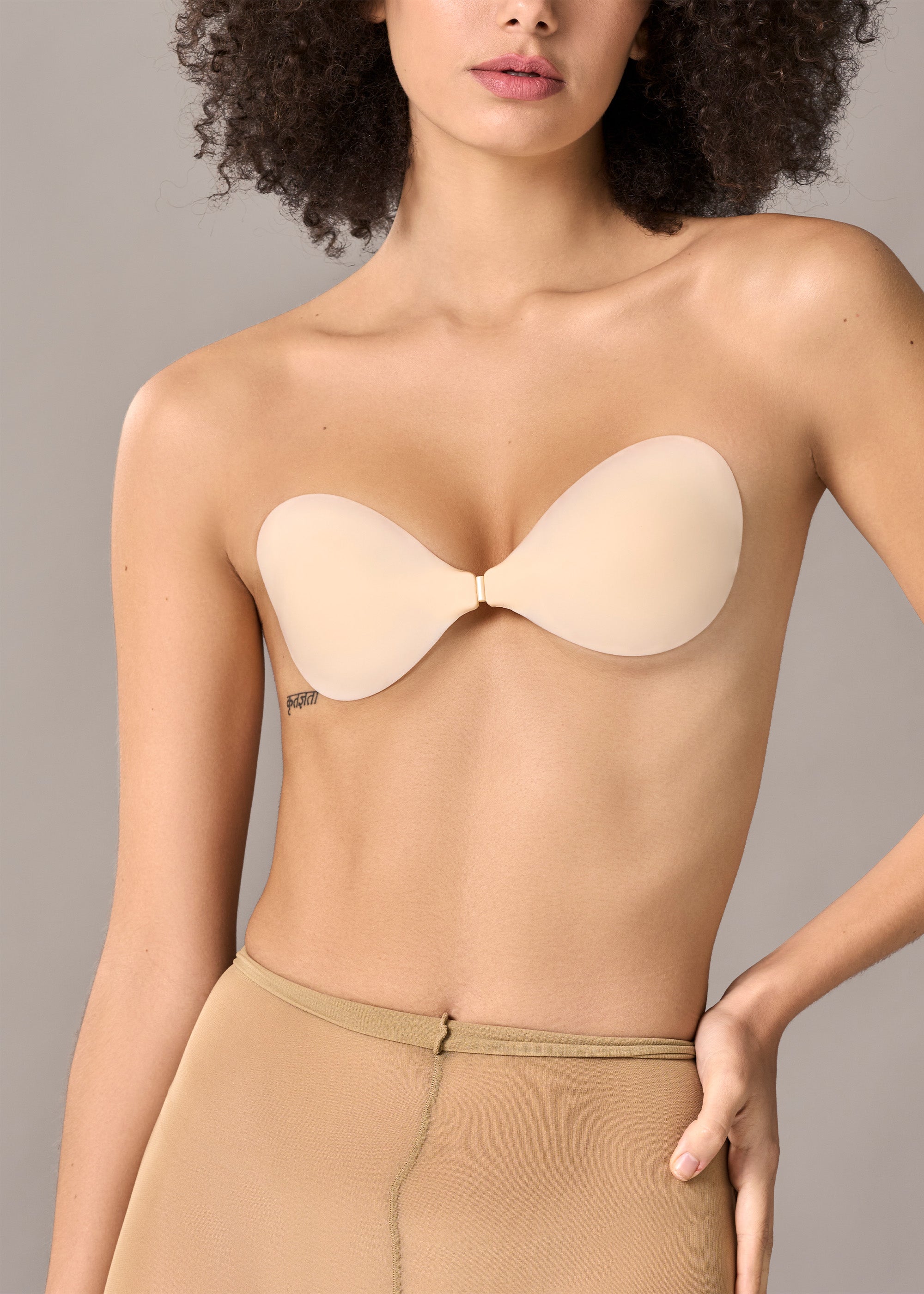 Woman wearing a beige strapless bra against a neutral background