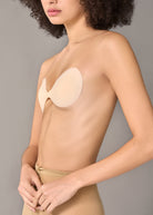 Close-up side view of a woman wearing a light beige bra and matching underwear against a plain gray studio background.
