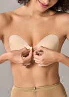 Woman applying a beige adhesive bra pad on a plain background