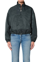 Person wearing a dark green jacket and light blue jeans on a white background