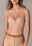 Close-up of a woman wearing a seamless, adhesive bra in a nude beige shade, with a front hook closure against a neutral gray background.