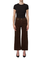 Person wearing a black top and brown wide-leg pants on a white background