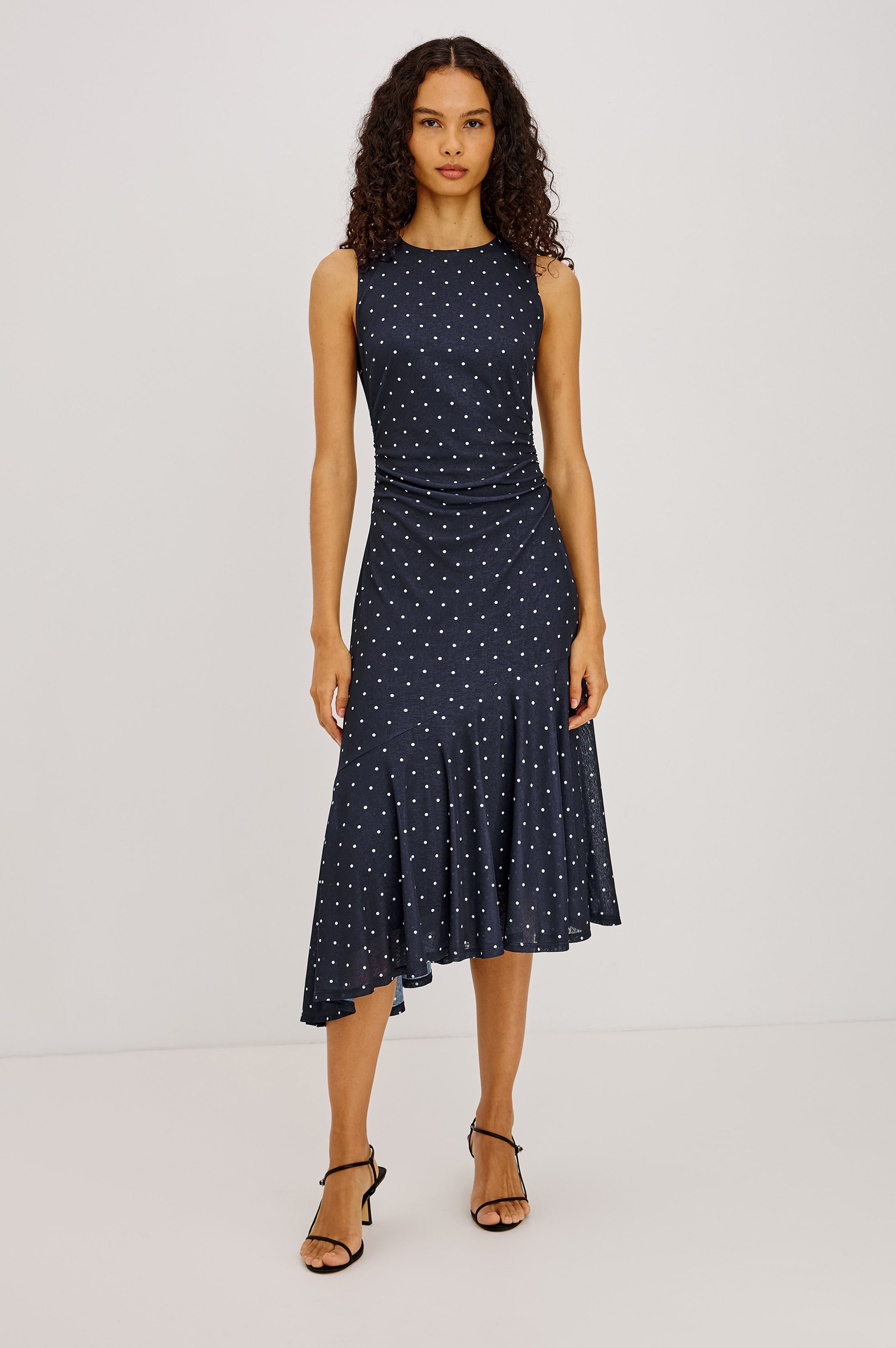 Woman wearing a navy dress with white polka dots on a white background