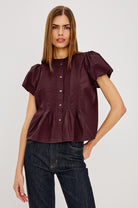 Woman wearing a burgundy blouse with puff sleeves and dark jeans on a light gray background