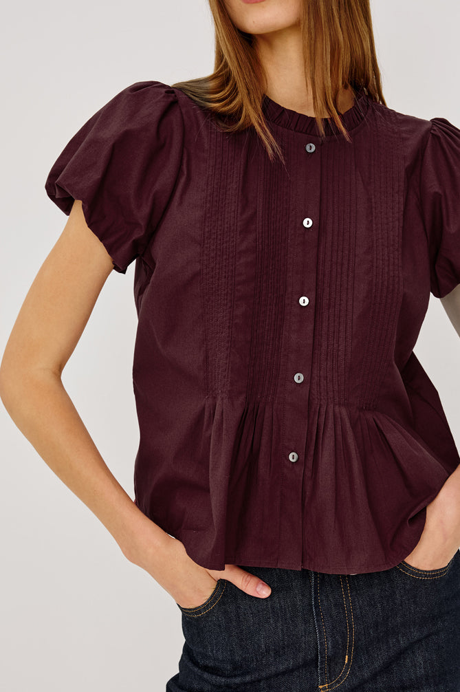 Woman wearing a burgundy blouse with puffed sleeves on a plain background