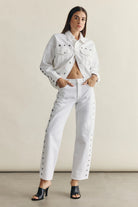 Woman wearing a white denim outfit with studded details against a neutral background