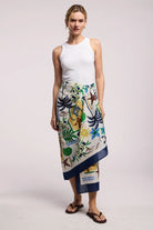 Woman wearing a white sleeveless top and colorful patterned skirt on a plain background