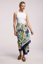 Woman wearing a white top and a colorful floral skirt on a plain background