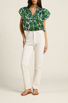 Woman wearing a green floral top and white pants on a beige background