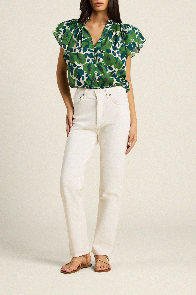 Woman wearing a green floral top and white pants on a beige background