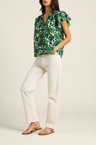 Woman wearing a green floral blouse and white pants on a plain background
