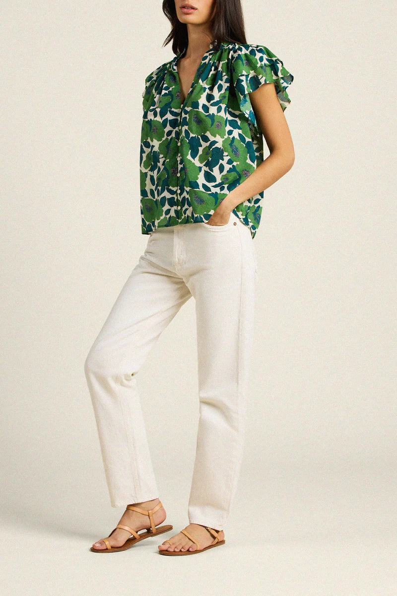 Woman wearing a green floral blouse and white pants on a plain background