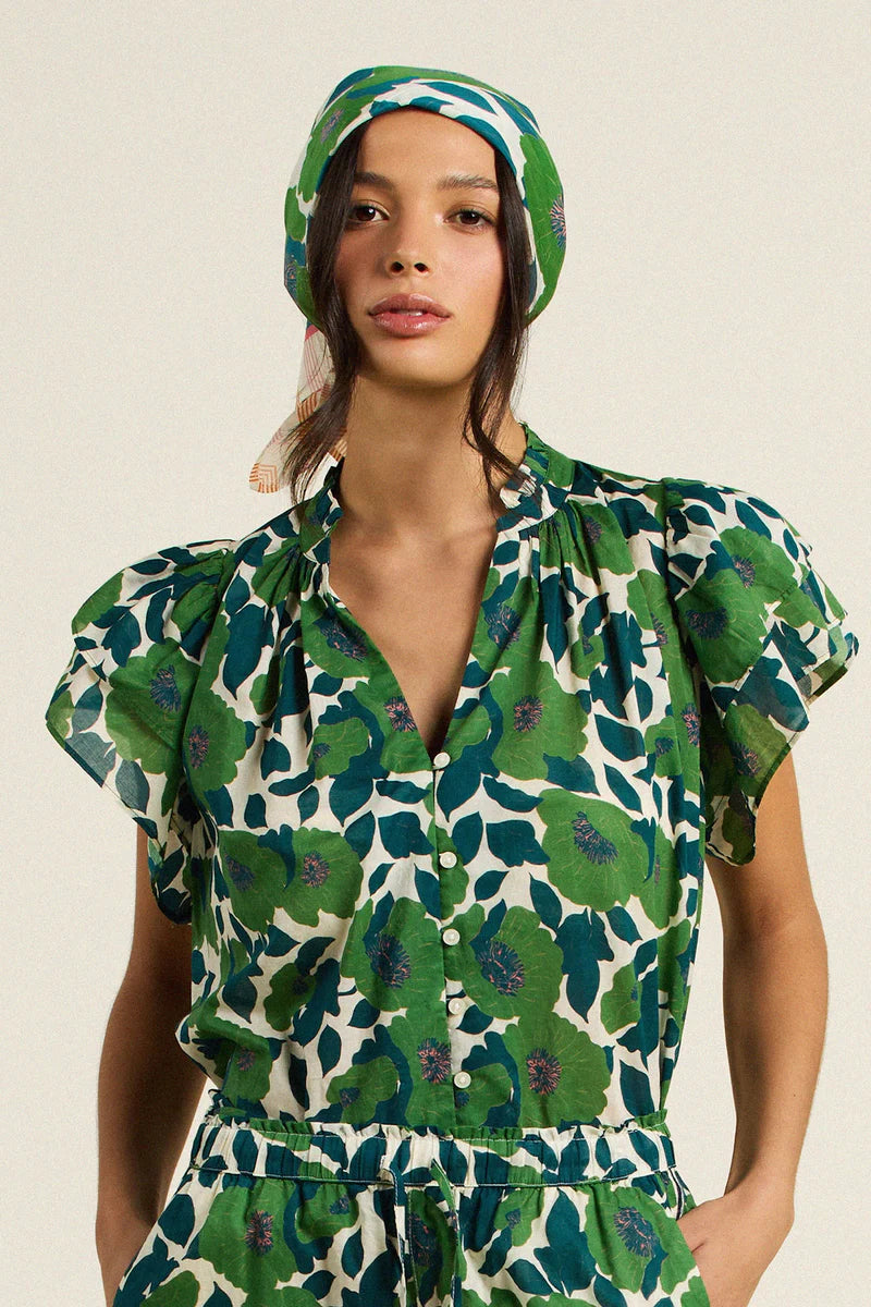 Woman wearing a green floral outfit with a matching headscarf on a beige background