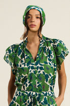 Woman wearing a green floral outfit with a matching headscarf on a beige background