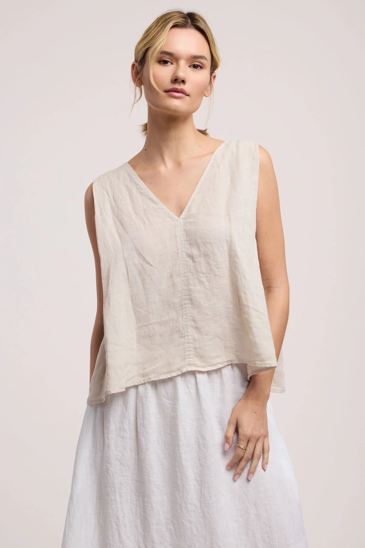 Woman wearing a light-colored sleeveless top and skirt against a plain background