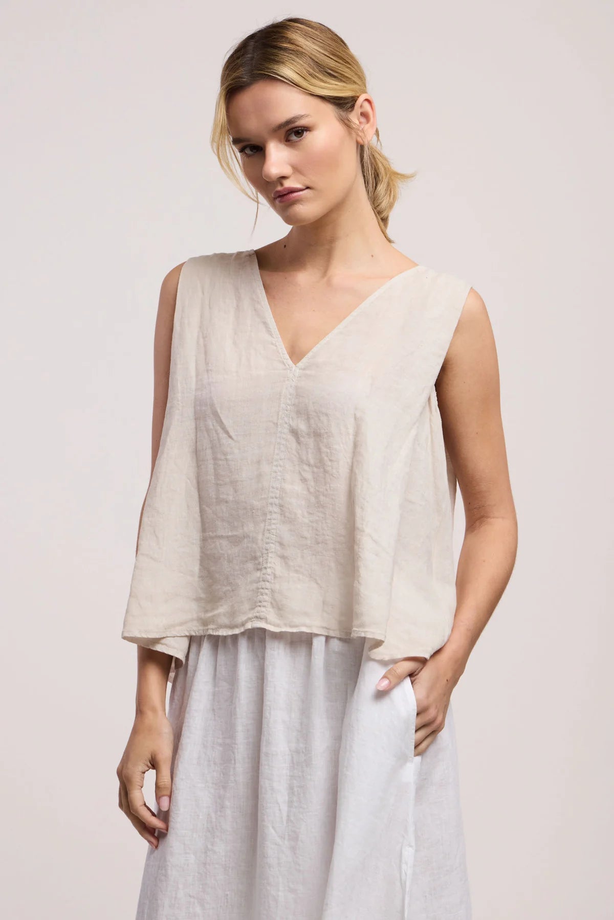 Woman wearing a beige sleeveless top and light gray pants on a plain background