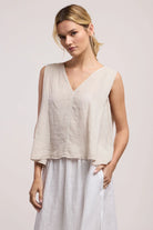 Woman wearing a beige sleeveless top and light gray pants on a plain background