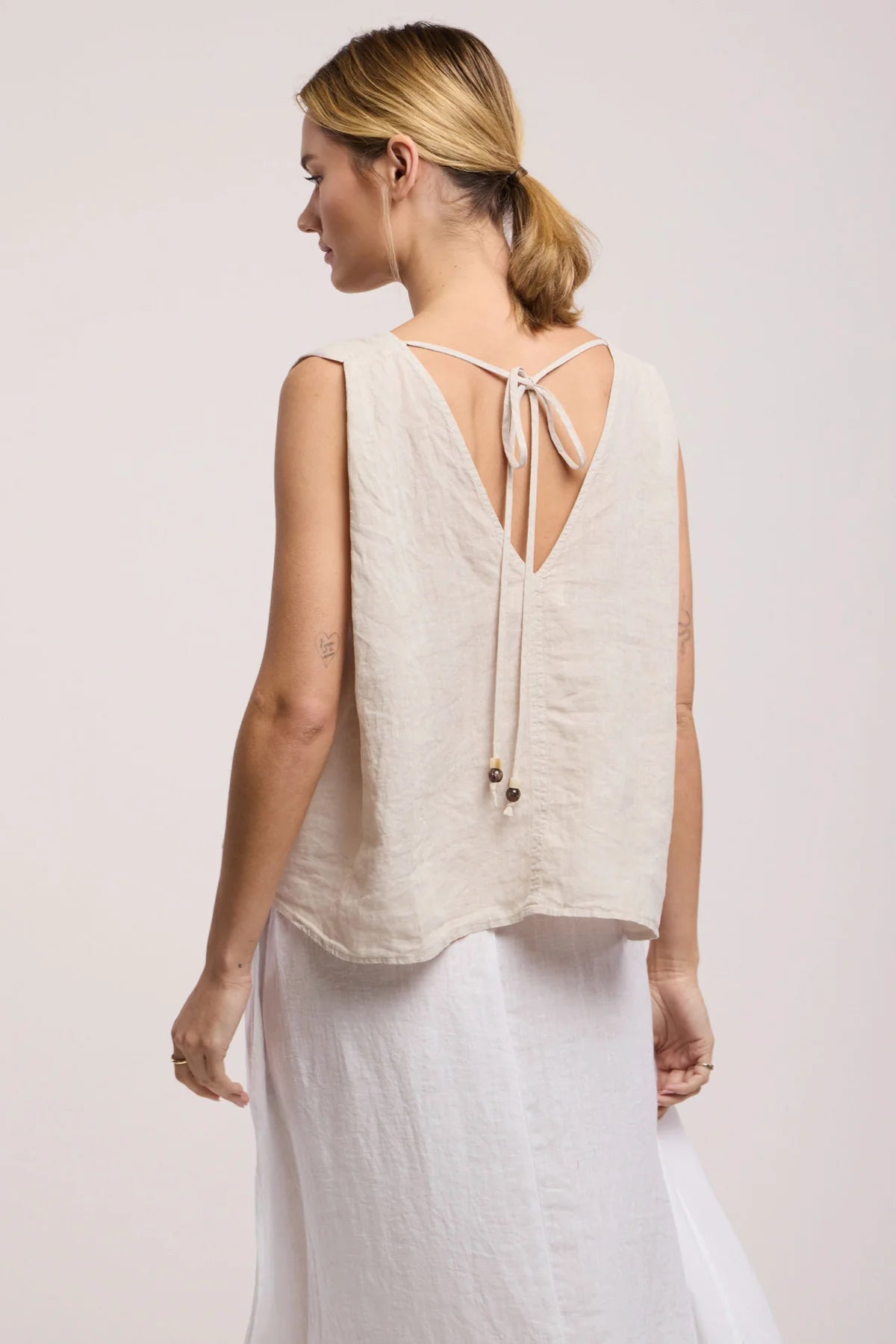 Woman wearing a beige sleeveless top with a tie back detail on a light pink background