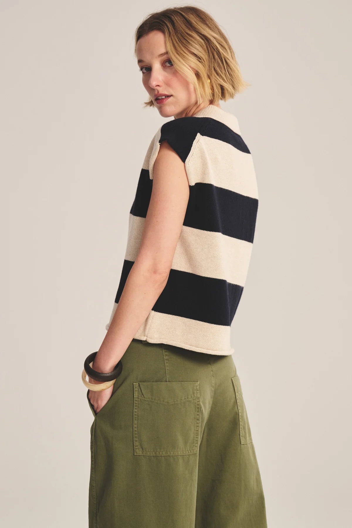 Woman wearing a black and white striped sleeveless top with green pants on a plain background